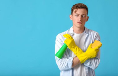 Mavi arka planda sünger ve deterjanı olan yakışıklı bir adam.