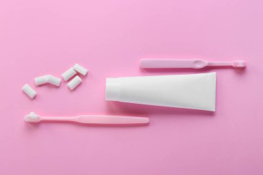 Diş macunlu tüp, fırçalar ve pembe arka planda lezzetli diş etleri.