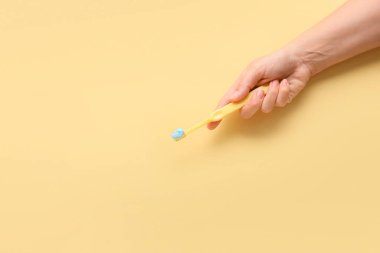 Bej arka planda diş fırçası ve yapıştırıcısı olan bir kadın eli.