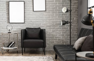 Lambalı kahve masası, kitaplar ve tuğla duvarın yanındaki siyah koltuk.