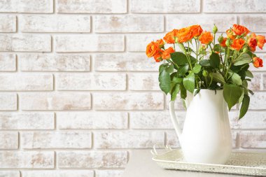 Tuğla duvara karşı güzel turuncu güllerle dolu bir sürahi.