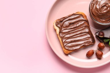 Bir tabak çikolatalı ekmek ve pembe arka planda fındıklar, yakın plan.