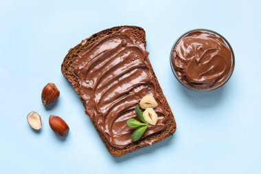 Çikolata ezmeli ekmek ve mavi arka planda fındık.