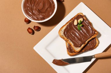 Çikolata ezmeli bir tabak ekmek ve bej arka planda fındık.