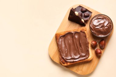 Çikolata ezmeli ekmek tahtası ve bej arka planda fındık.