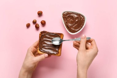Kadın, çikolata ezmeli lezzetli tost ve pembe arka planda fındık hazırlıyor.