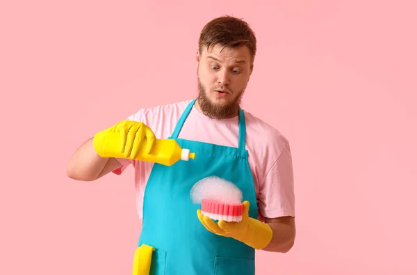 ピンクの背景にスポンジに洗剤を注ぐショックを受けた若い男 — ストック写真