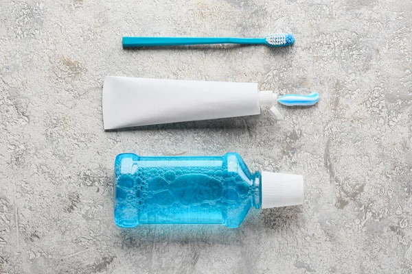 Tube with tooth paste, brush and mouthwash on grey background