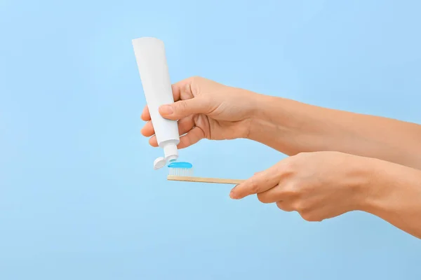 Woman squeezing tooth paste onto brush on blue background