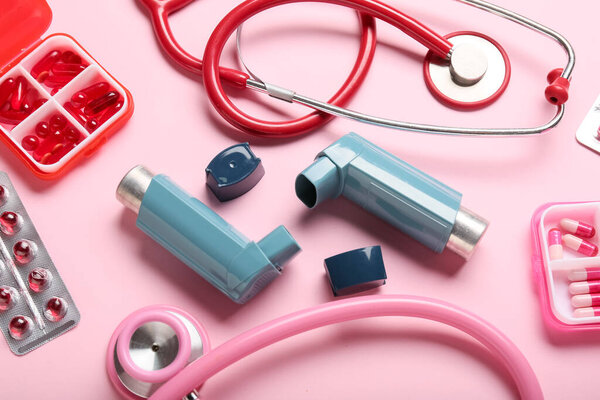 Asthma inhalers, stethoscopes and pills on pink background, closeup