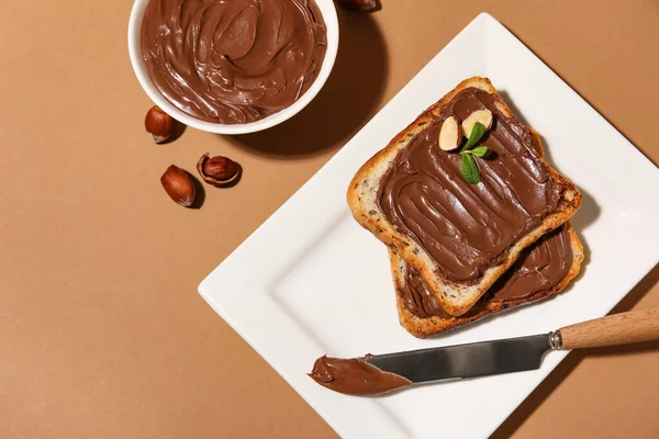 Çikolata ezmeli bir tabak ekmek ve bej arka planda fındık.