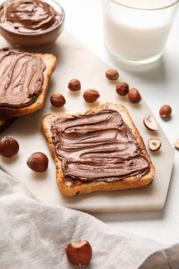 Çikolata ezmeli ekmek tahtası ve beyaz arka planda fındık.