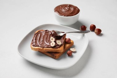 Çikolata ezmeli bir tabak ekmek ve beyaz arka planda fındık.