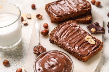 Çikolata ezmeli ekmek, fındık ve arka planda bir bardak süt.
