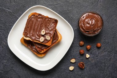 Çikolata ezmeli bir tabak ekmek ve siyah arka planda fındık.