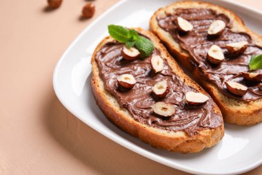 Bir tabak çikolatalı ekmek ve bej arka planda fındık, yakın plan.