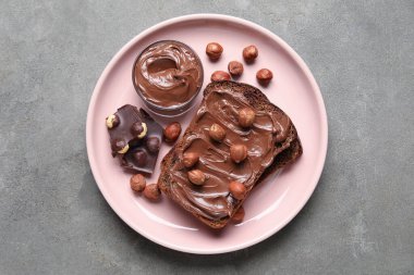 Çikolata ezmeli bir tabak ekmek ve gri arka planda fındık.