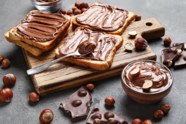 Çikolata ezmeli ahşap tahta tahta ve gri arka planda fındık.