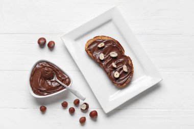 Çikolata ezmeli bir tabak ekmek ve beyaz ahşap arka planda fındık.