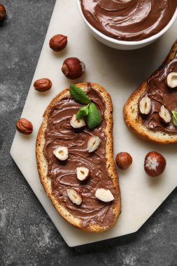 Çikolata ezmeli ekmek tahtası ve siyah arka planda fındık, yakın plan.