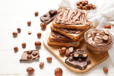 Çikolata ezmeli ekmek tahtası ve beyaz ahşap arka planda fındık.