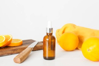 Bir şişe temel yağ ve taze portakallar açık ahşap masada.