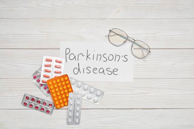 Kağıt levha, metin Parkinson hastalığı ve beyaz ahşap arka planda haplar