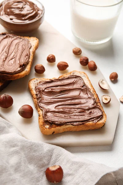 Çikolata ezmeli ekmek tahtası ve beyaz arka planda fındık.