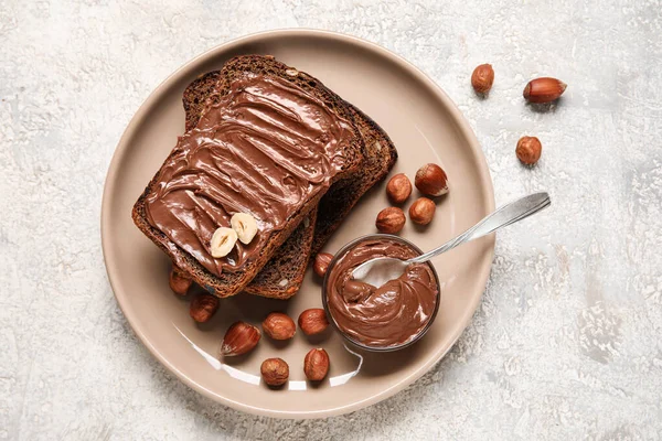 Çikolata ezmeli bir tabak ekmek ve arka planda fındık.