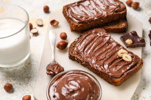 Çikolata ezmeli ekmek, fındık ve arka planda bir bardak süt.