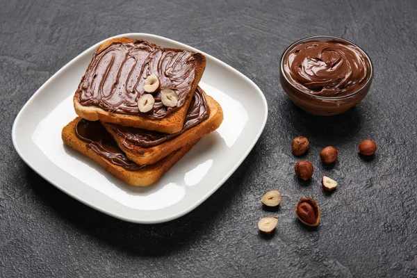 Çikolata ezmeli bir tabak ekmek ve siyah arka planda fındık.