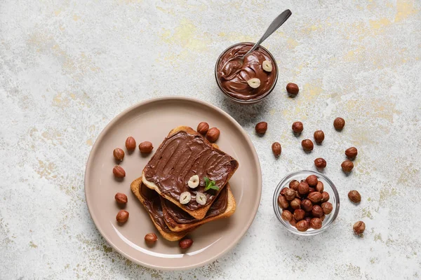 Çikolata ezmeli bir tabak ekmek ve arka planda fındık.