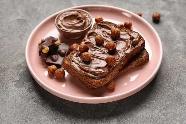 Çikolata ezmeli bir tabak ekmek ve gri arka planda fındık.