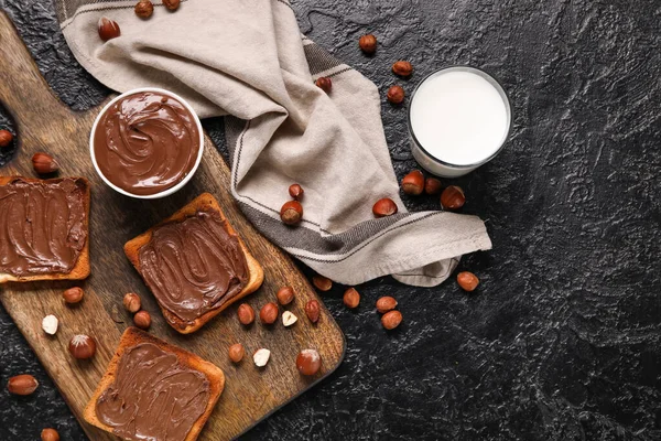 Çikolata ezmeli ekmek, fındık ve siyah arka planda bir bardak süt.