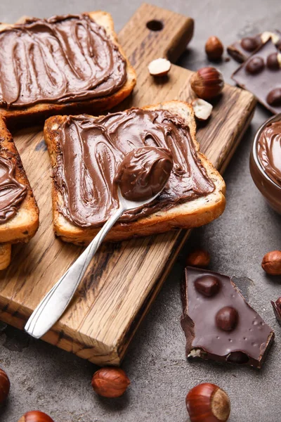 Çikolata ezmeli ahşap tahta tahta ve gri arka planda fındık.