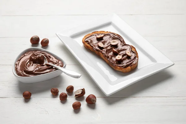 Plate of bread with chocolate paste and hazelnuts on white wooden background