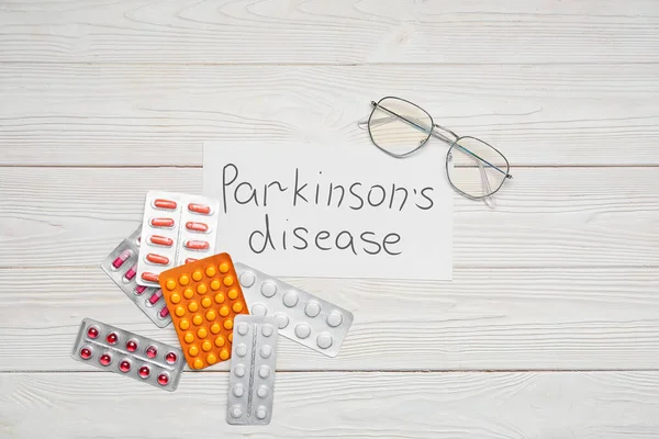 Kağıt levha, metin Parkinson hastalığı ve beyaz ahşap arka planda haplar