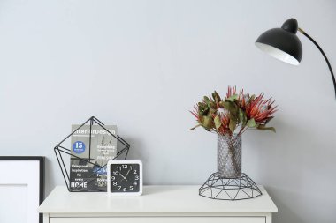 Çiçekli vazo, şarjör ve saat ışıklı duvarın yanında.