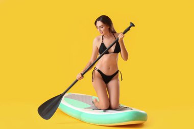 Sörf tahtası olan genç bir kadın ve renkli arka planda kürek çeken.