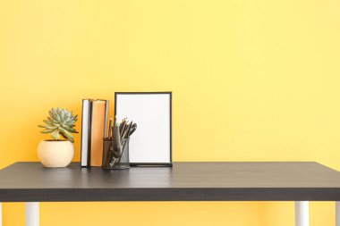 Kırtasiye sahibi, ev bitkisi, kitaplar ve renk duvarına yakın boş fotoğraf çerçevesi olan işyeri