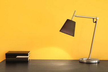 Renk duvarının yanındaki masada parlayan lamba ve kitap yığını