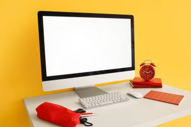 Modern bilgisayar, kırtasiye malzemeleri ve alarm saati renkli duvarın yanındaki masada.