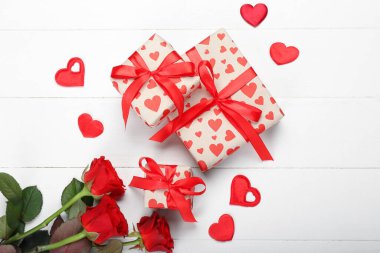 Beyaz ahşap arka planda Sevgililer Günü için güzel güller ve hediye kutuları
