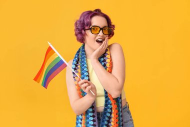 Sarı arka planda LGBT bayrağı olan şaşırmış genç bir kadın.