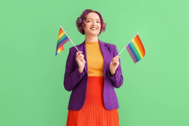 Yeşil arka planda LGBT bayrakları olan genç bir kadın.
