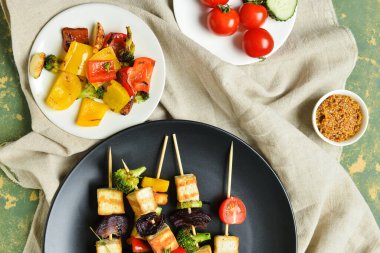 Renkli arkaplanda kızarmış tofu peynirli şiş ve sebzeli kompozisyon