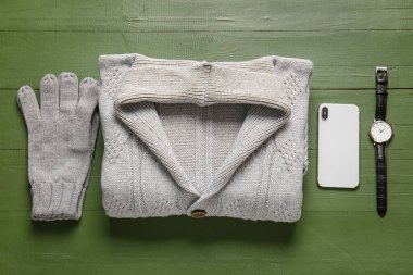 Erkek süveter, eldiven, kol saati ve yeşil ahşap arka planda cep telefonu.