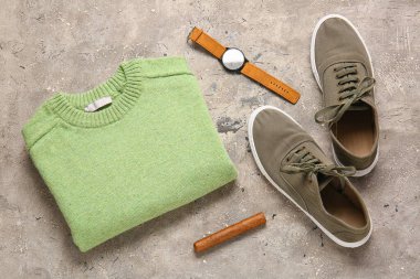 Erkek süveteri, ayakkabılar, kol saati ve grunge arka planda puro.