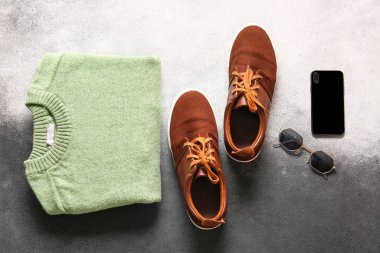Beyaz ve siyah arkaplanda erkek kazağı, ayakkabı, güneş gözlüğü ve cep telefonu