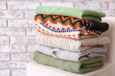 Hafif tuğlalı arka plana karşı puf üzerine şık süveter yığını, yakın plan